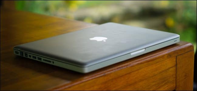 An old, thick MacBook Pro sitting on a wooden desk.